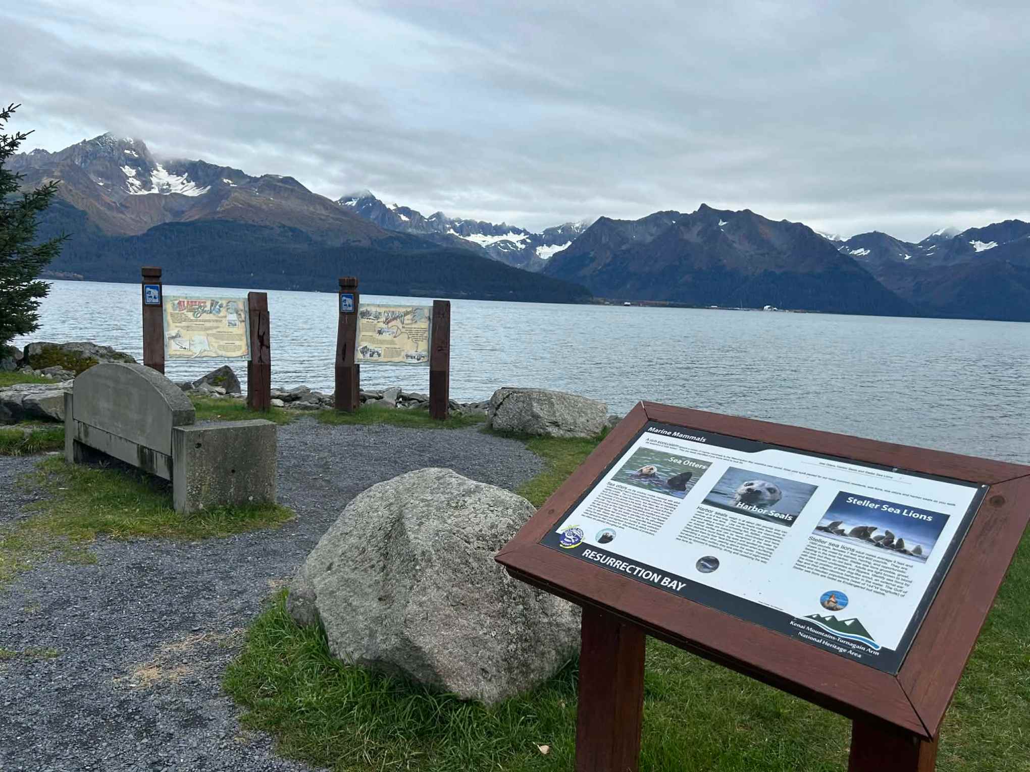 Scenic view of Resurrection Bay with interpretive signs and snow-capped mountains in the background.