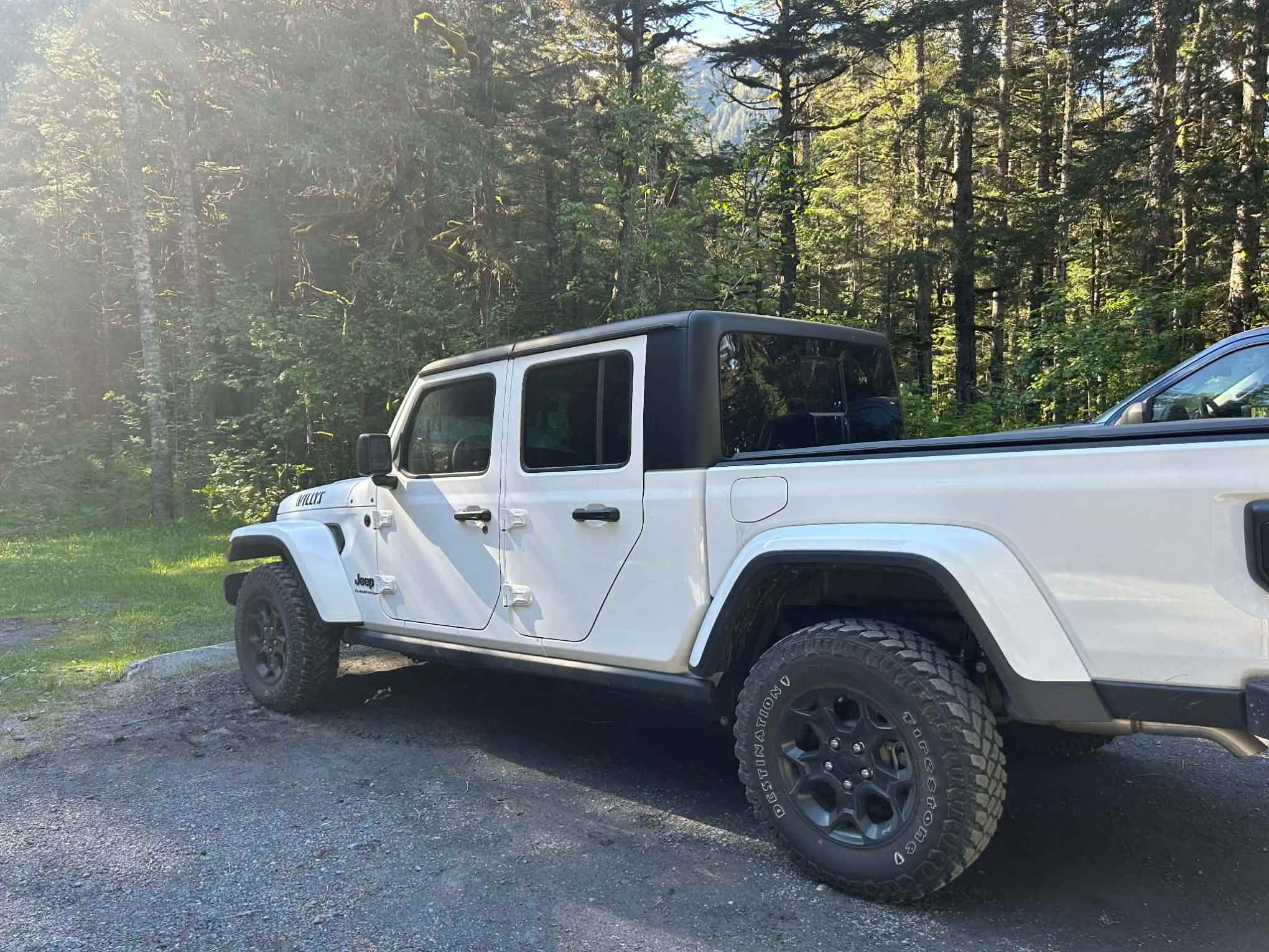 White off-road vehicle parked on a gravel area surrounded by trees.