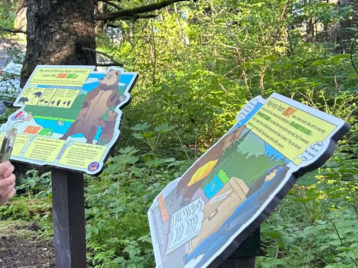 Two informational signs in a forested area with trees and greenery.