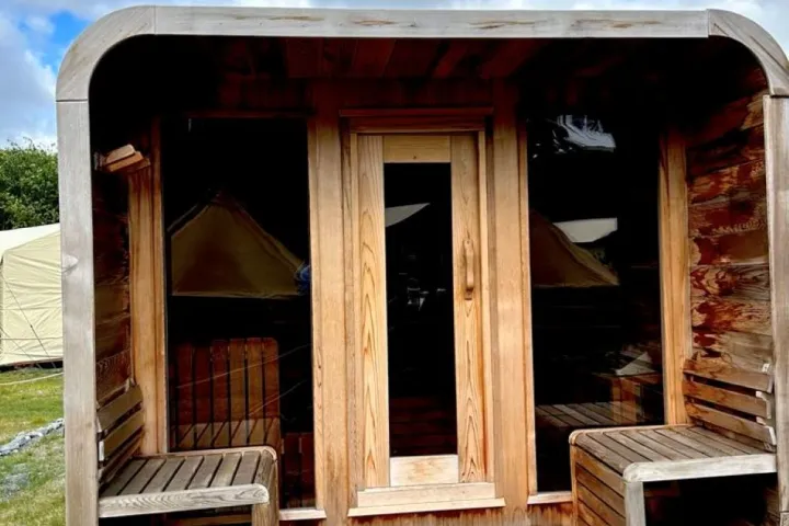 Small wooden structure with glass door and benches, set outdoors under cloudy sky.
