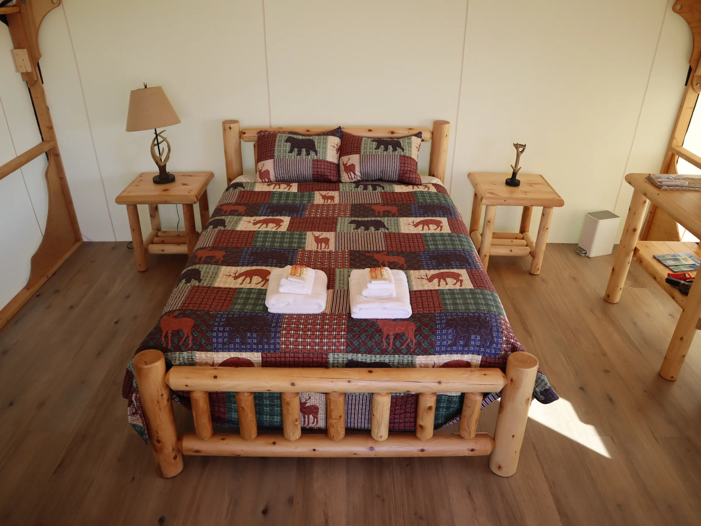 Rustic bedroom with log bed, patchwork quilt, and wooden furniture on a wooden floor.