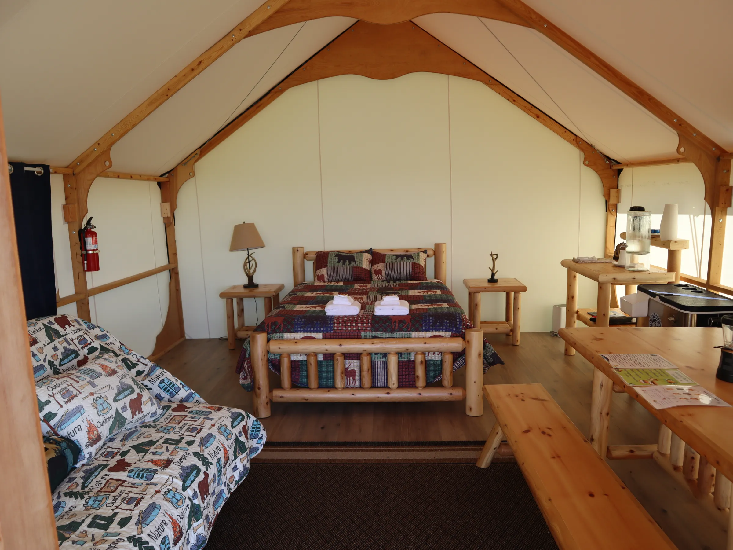 Glamping tent interior with wooden furniture, a bed, and a table.