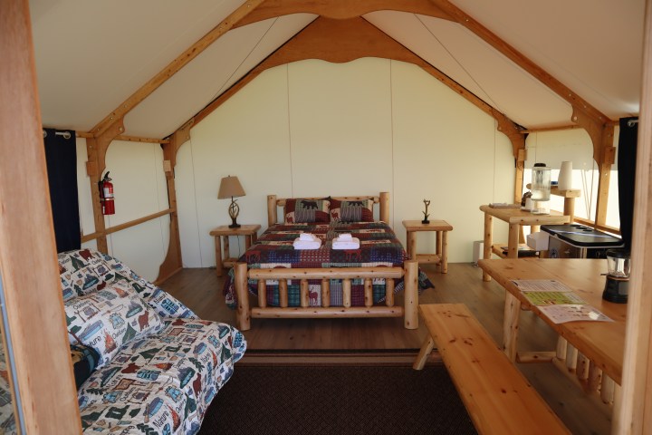 Glamping tent interior with wooden furniture, a bed, and a table.