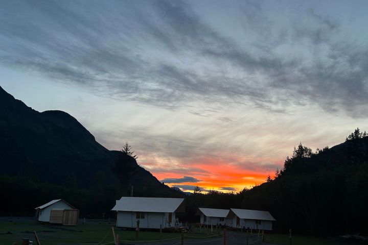 Mountain sunset with colorful sky above cabins and trees.
