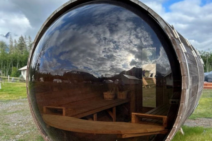 Barrel-shaped building with reflective glass, cloudy sky reflection, and wooden interior benches.