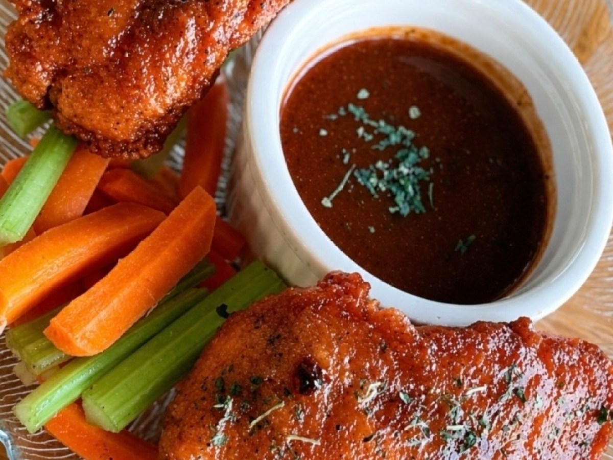 Two fried chicken pieces with dipping sauce and carrot, celery sticks on a plate.