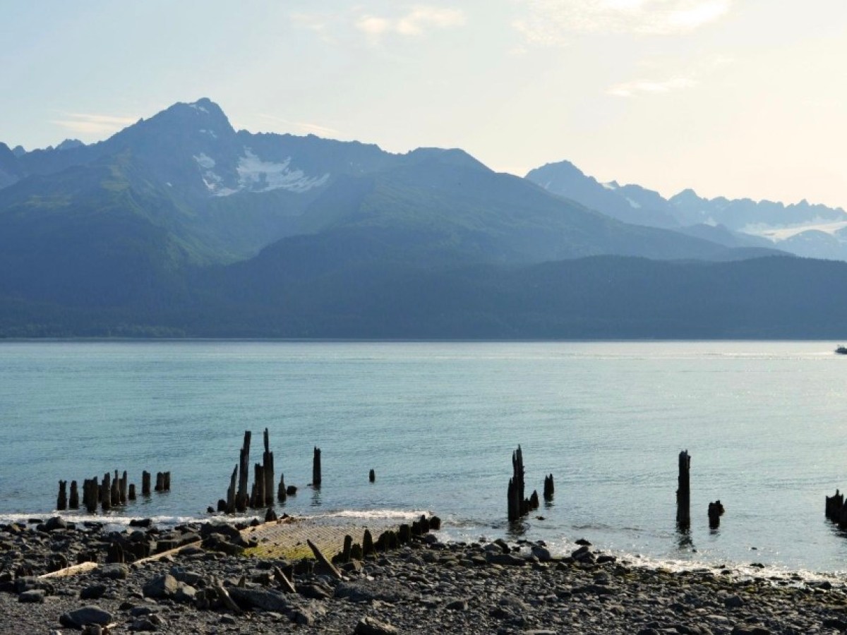 Calm lake with wooden posts and mountain range in the background.