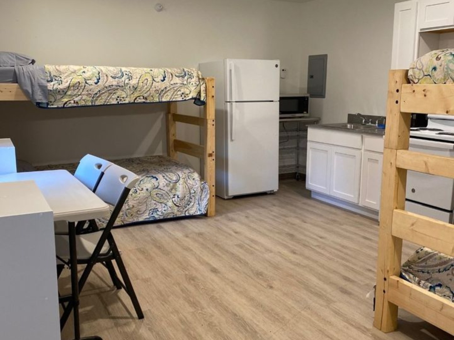 Room with bunk beds, table, chairs, refrigerator, microwave, and cabinets.
