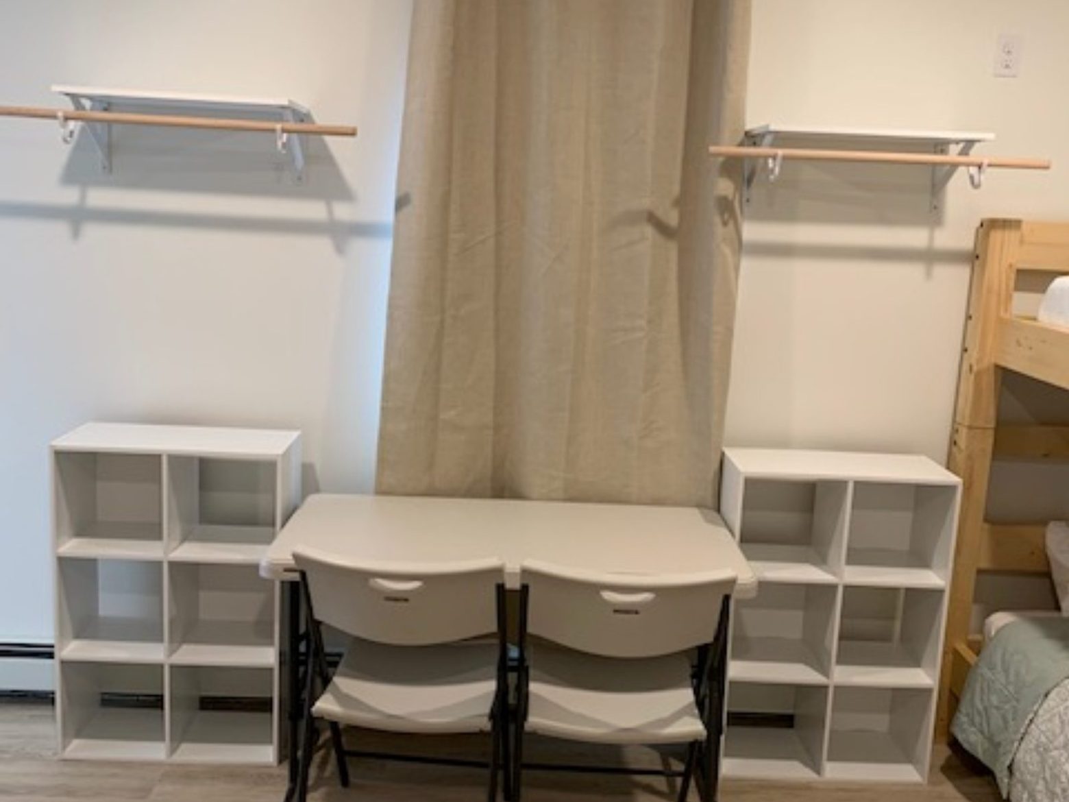 Room with two chairs at a desk, shelves, and beige curtains on a wood floor.