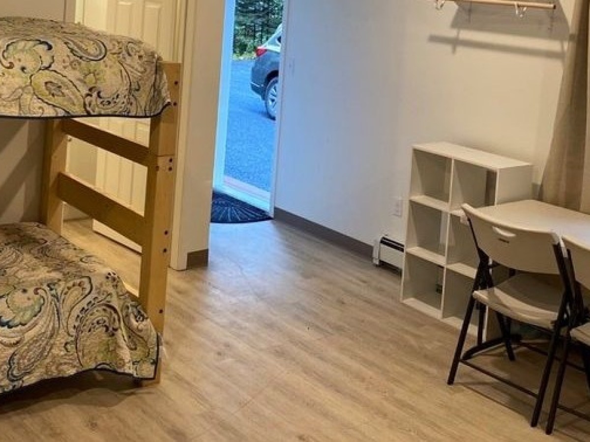 Room with bunk bed, table, chairs, and open door showing a car outside.