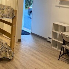 Room with bunk bed, table, chairs, and open door showing a car outside.