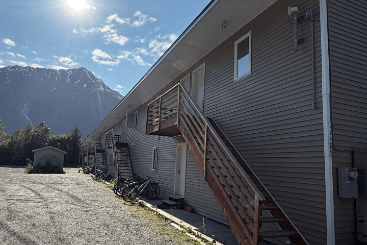 Apartment building with external stairs, bicycles, and mountain in background under a sunny sky.
