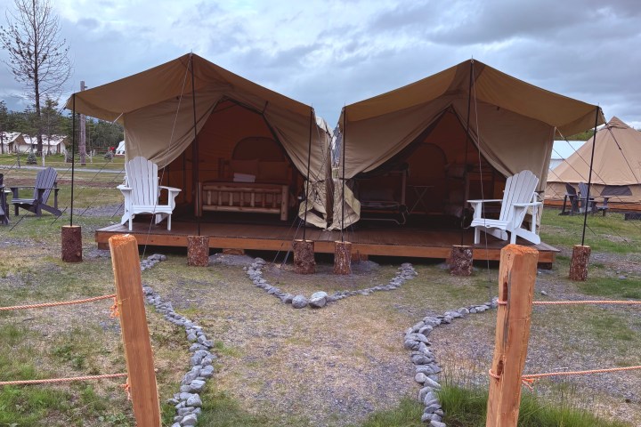 Two canvas tents with chairs on a wooden deck under a cloudy sky.