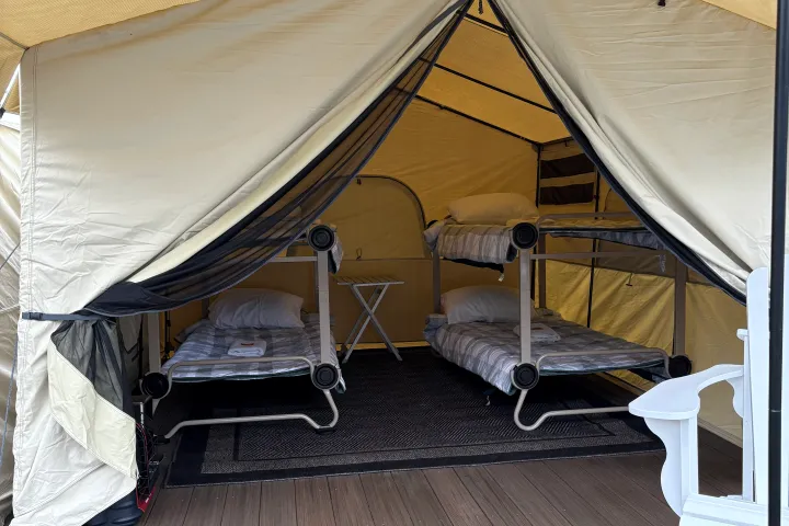 Canvas tent with two bunk beds, a small table, and a wooden deck.