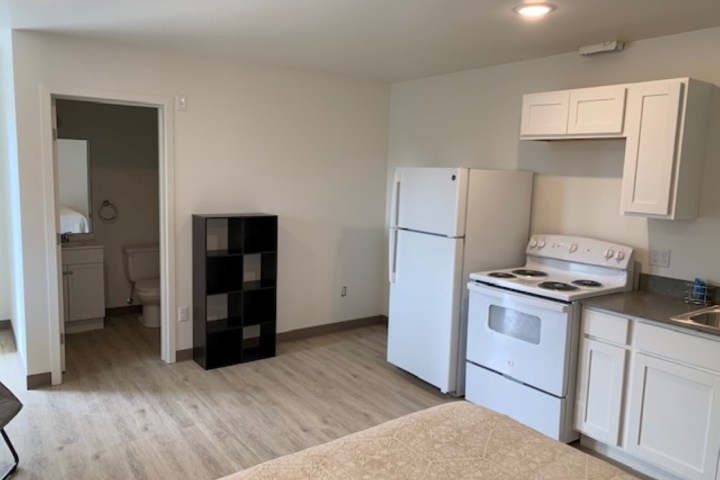 Small apartment kitchen with fridge, stove, and open bathroom door on left.