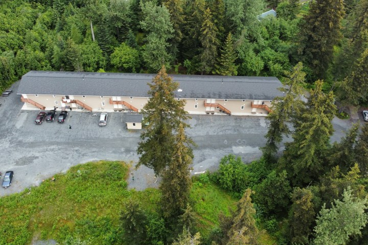 Aerial view of a long building with parked cars surrounded by dense trees.