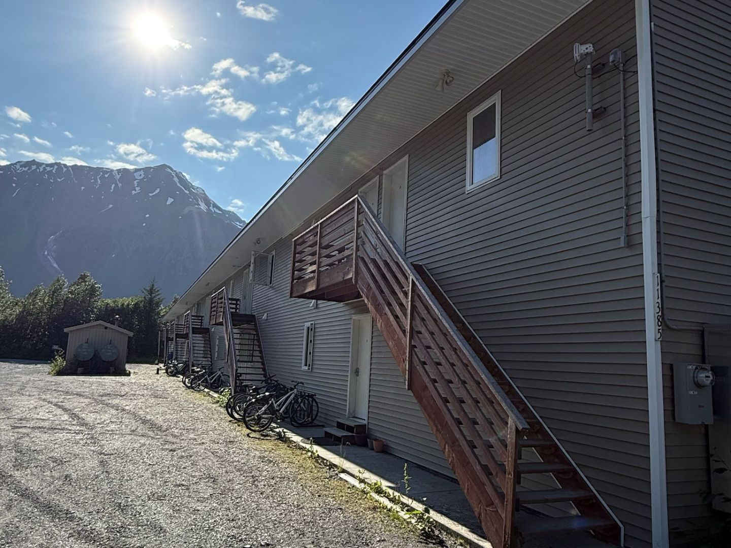 Side view of a building with stairs, bikes, sunny sky, and mountains in background.