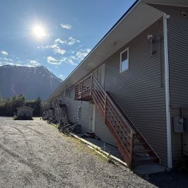 Side view of a building with stairs, bikes, sunny sky, and mountains in background.