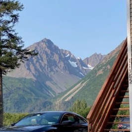 Car near wooden stairs with mountain and tree in background.