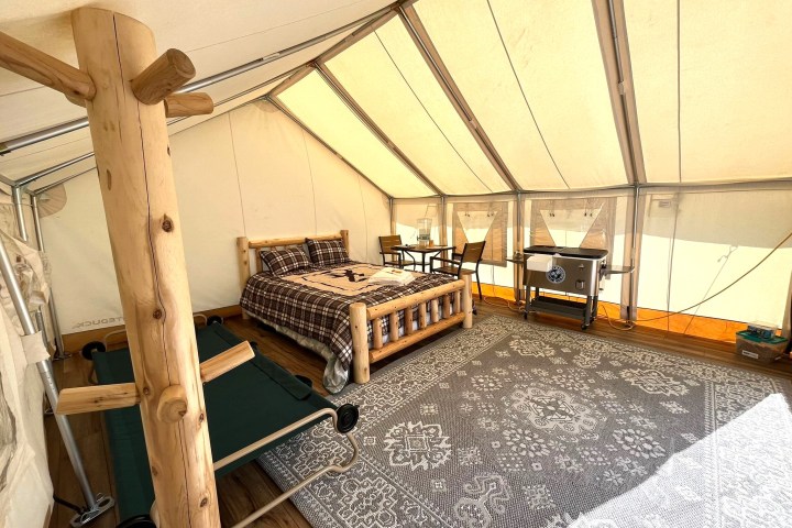 Interior of a glamping tent with a bed, a cot, a rug, and a small table with chairs.