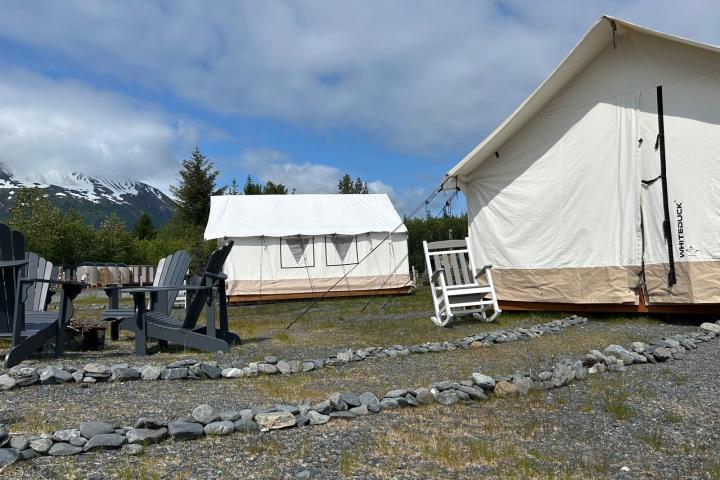 Canvas tents with chairs and a mountain backdrop under a cloudy sky.