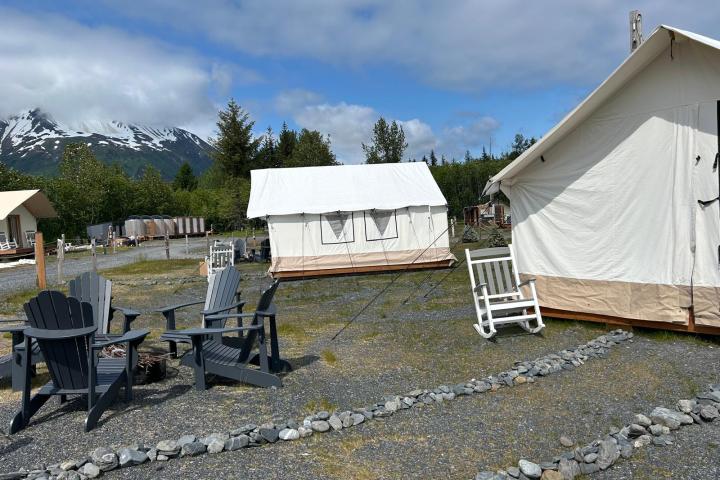 Tents and chairs at a campsite with mountain and trees in the background under a cloudy sky.