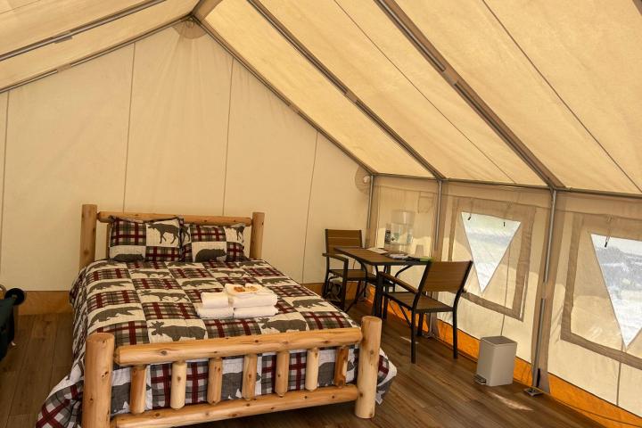 Cozy glamping tent with wooden bed, plaid bedding, and small dining area indoors.