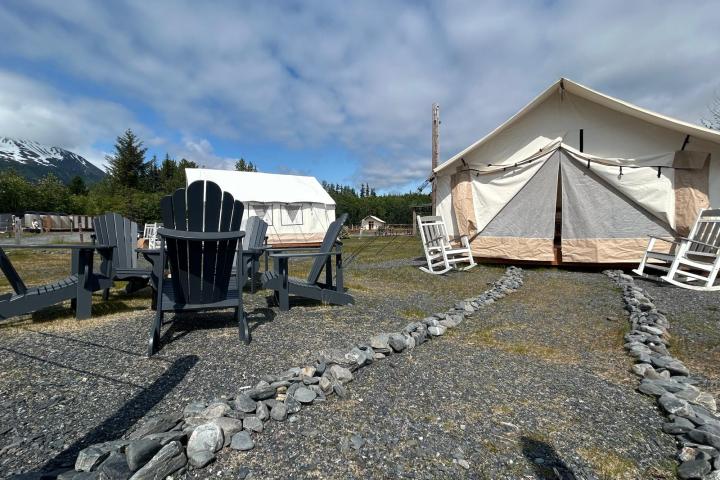 Outdoor camping site with canvas tents, Adirondack chairs, and a mountain in the background.