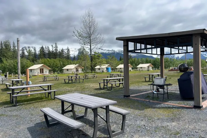 Outdoor campsite with picnic tables, tents, and a grill under a cloudy sky.