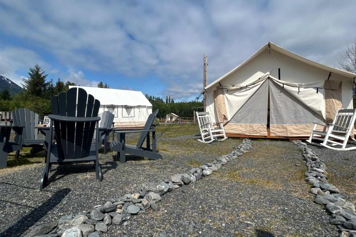 Two tents in a rural setting with chairs and a rocky path under a partly cloudy sky.