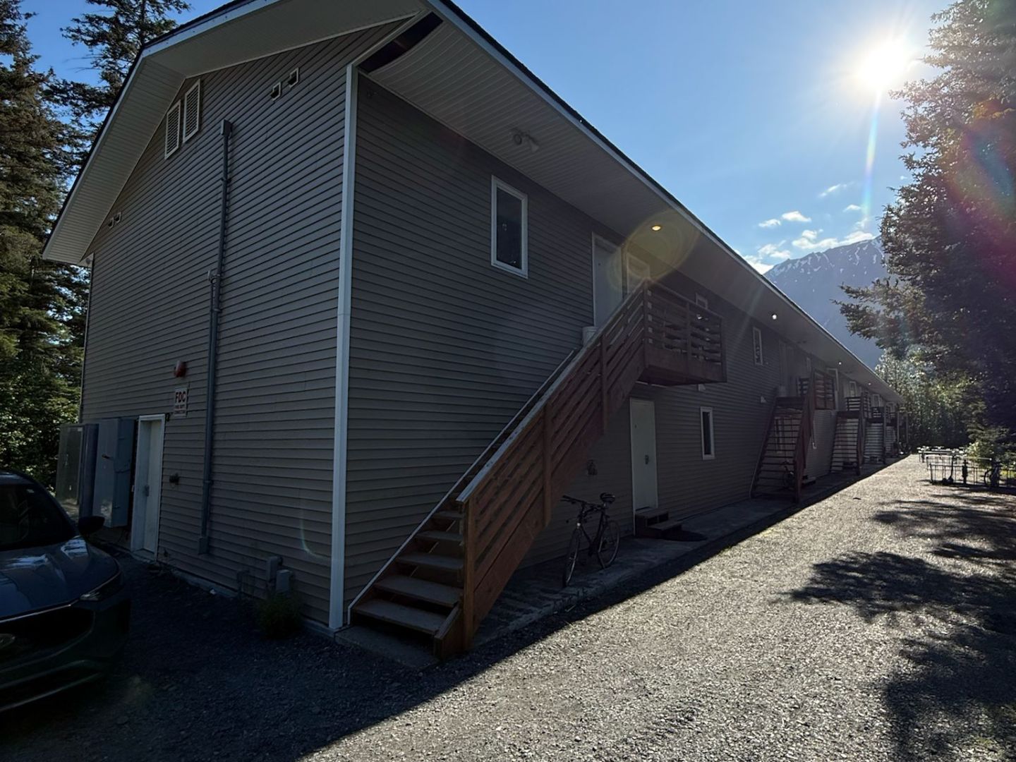 Apartment building with side stairs, gravel path, and bright sun in background.