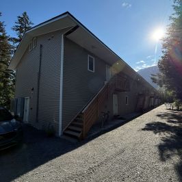Apartment building with side stairs, gravel path, and bright sun in background.