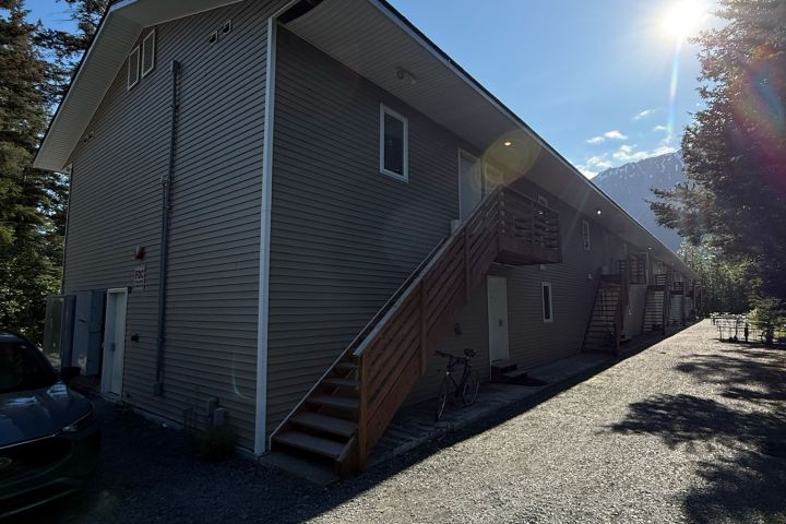 Apartment building with side stairs, gravel path, and bright sun in background.