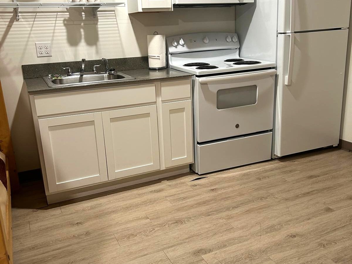 Small kitchen with white appliances, cabinets, and wooden floor.