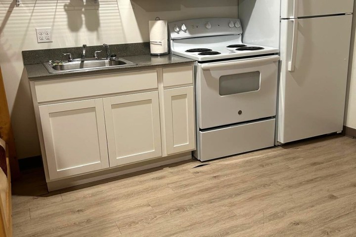 Small kitchen with white cabinets, oven, fridge, microwave, and wooden floor.