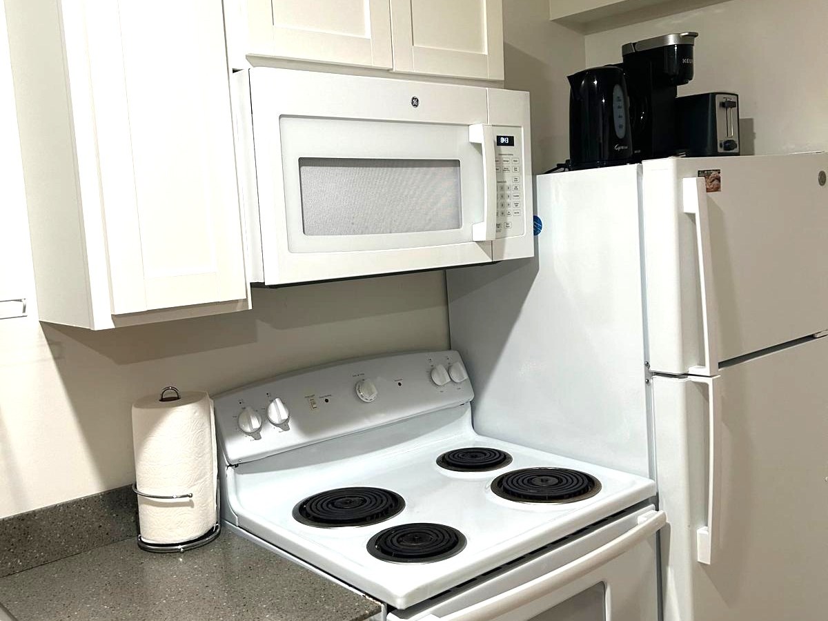 Compact kitchen with stove, microwave, fridge, and coffee maker.