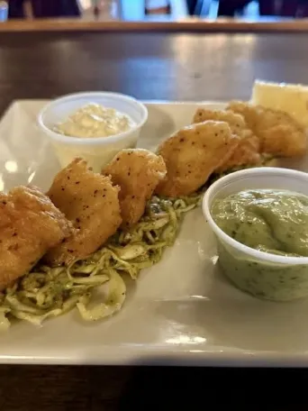 Fried shrimp on slaw with two sauce cups and lemon wedge on a square plate.