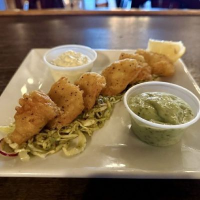Fried shrimp on slaw with two sauce cups and lemon wedge on a square plate.
