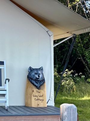 Wooden wolf sign reading 'The Grey Wolf Cottage' on porch near a folding chair.