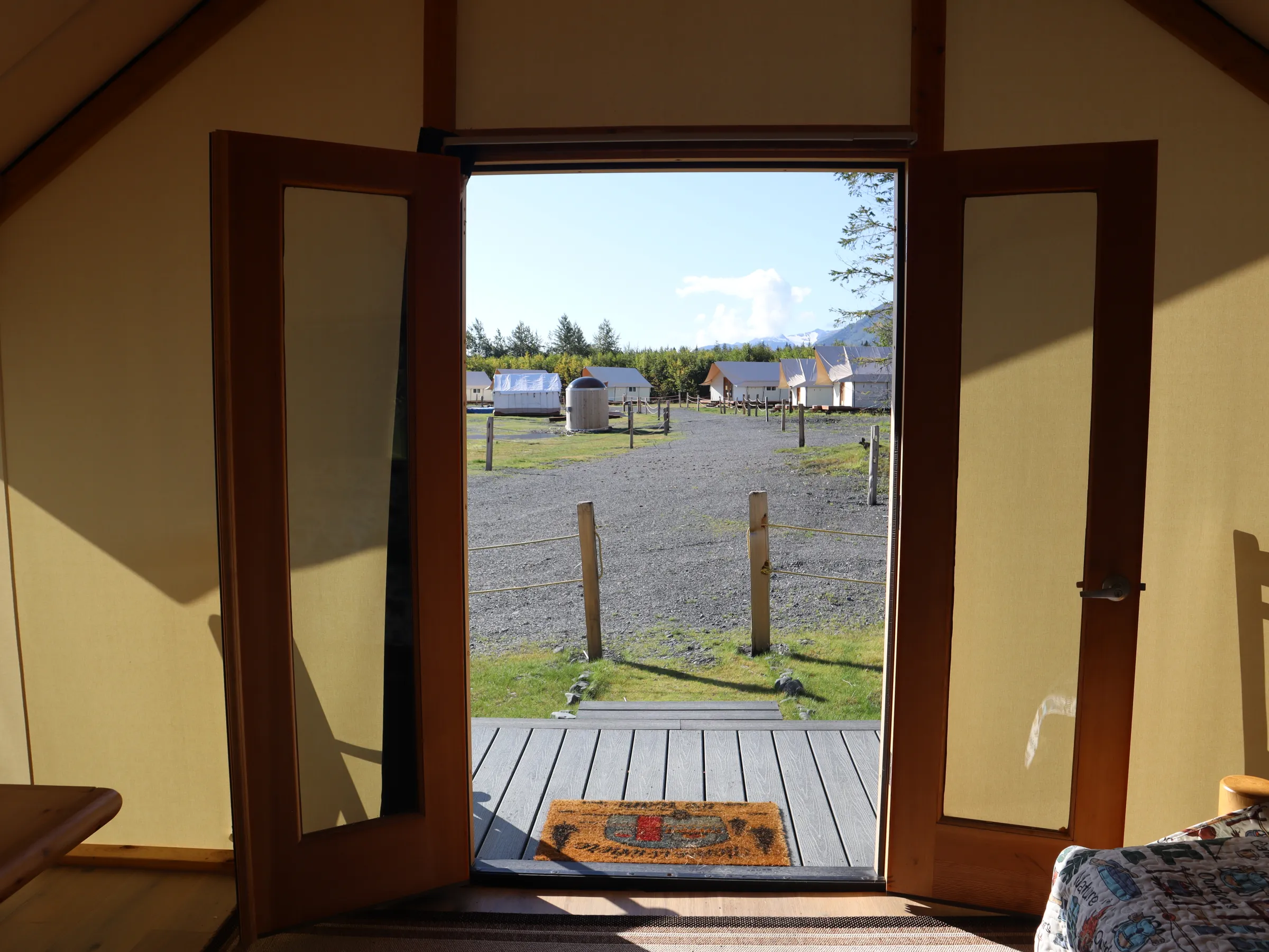 Open wooden door view of a campsite with tents and gravel path.