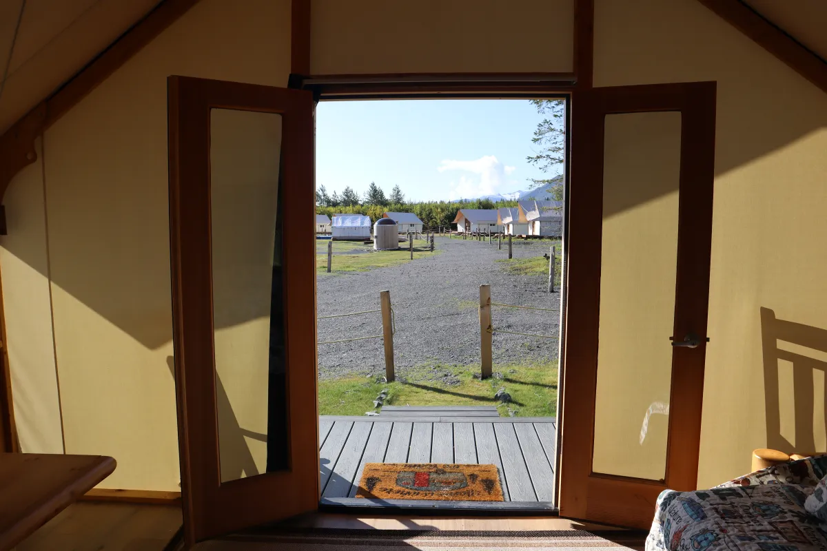 Open wooden door view of a campsite with tents and gravel path.