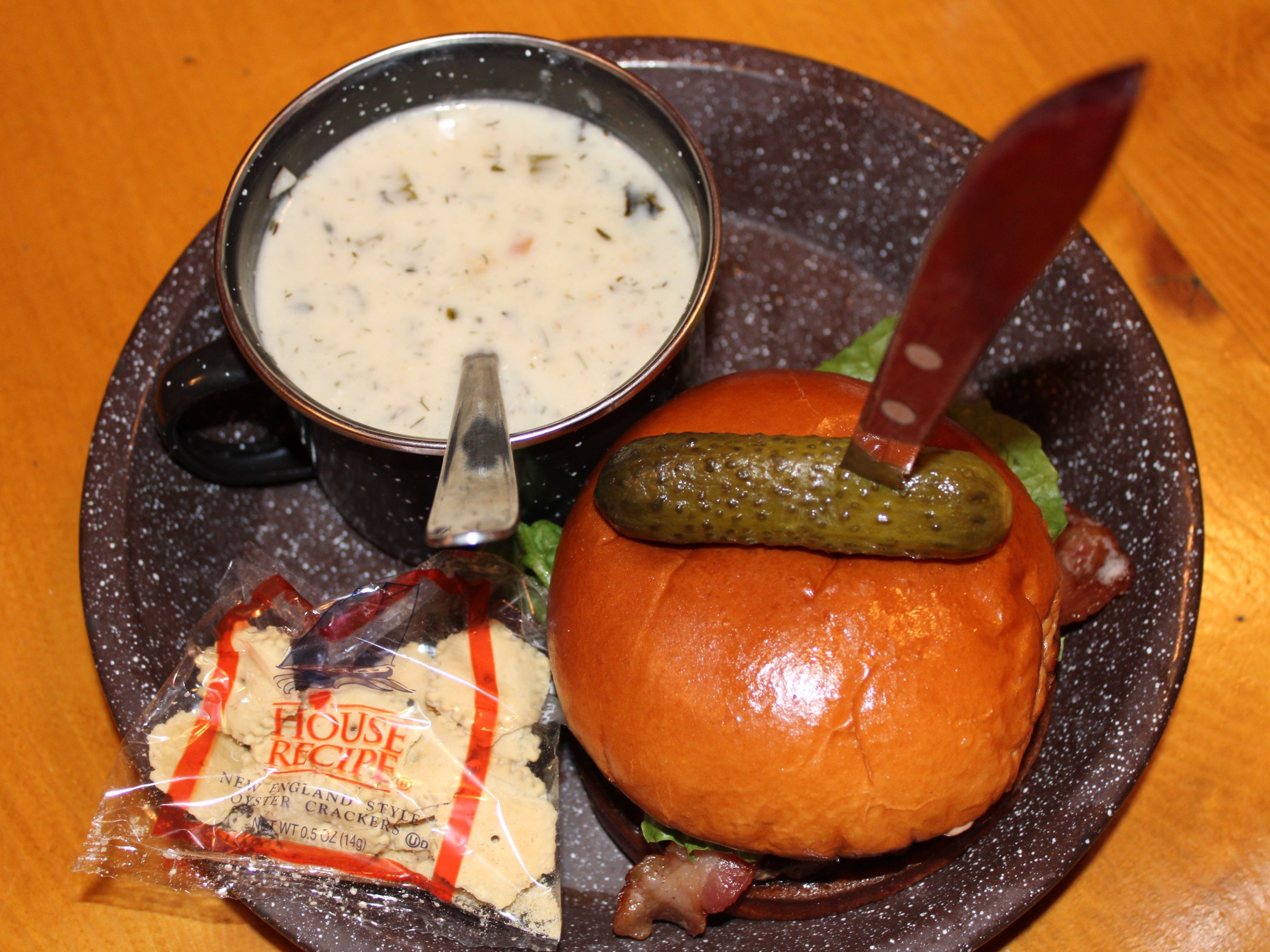 Bowl of soup, burger with pickle, and crackers on a plate.