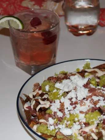 Loaded fries with cheese, bacon, and jalapeños. Cocktail with lime wedge in the background.