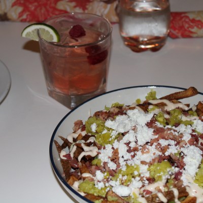Loaded fries with cheese, bacon, and jalapeños. Cocktail with lime wedge in the background.