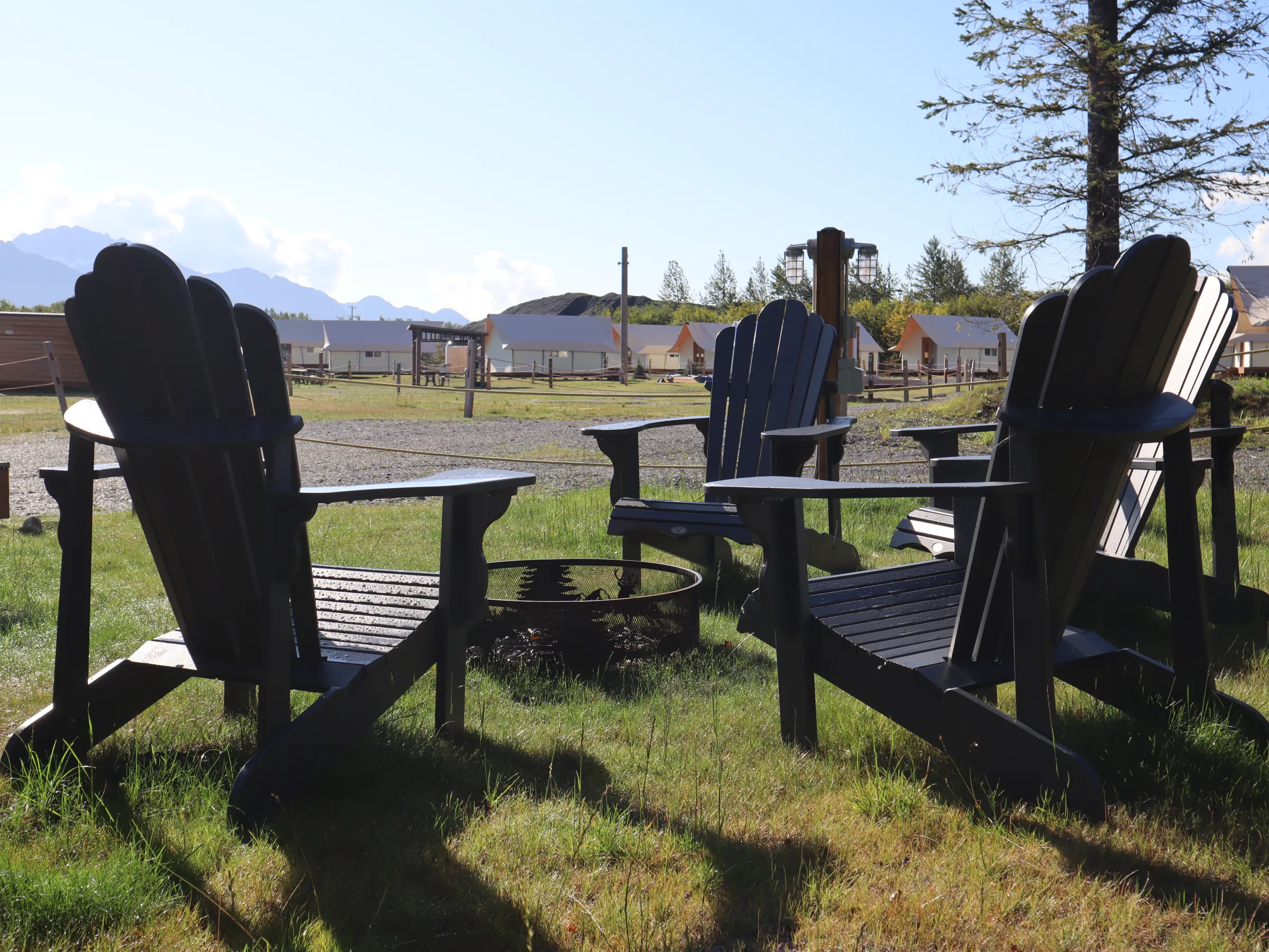 Four Adirondack chairs surround a fire pit in a grassy outdoor setting.