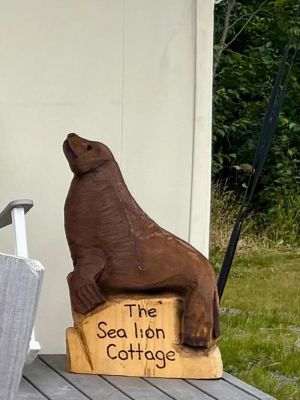Wooden sea lion sculpture with 'The Sea lion Cottage' sign on a porch.