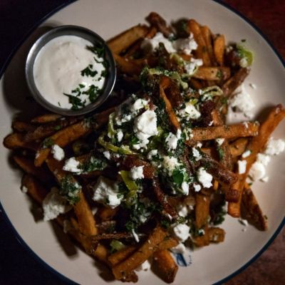 Plate of fries with cheese, herbs, and dip on the side on a wooden table.