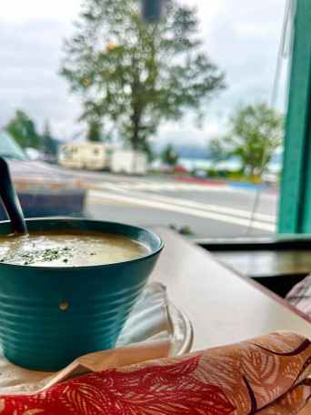 Blue bowl of soup on a table by a window with a tree and street view.