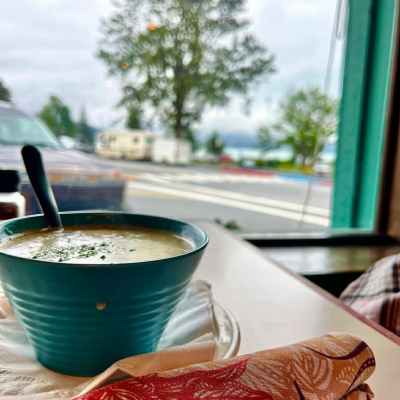 Blue bowl of soup on a table by a window with a tree and street view.