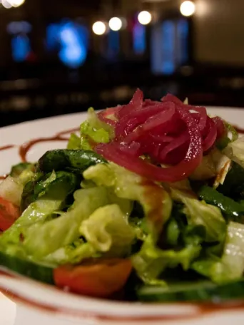 Mixed salad with pickled onions and balsamic glaze on white plate.